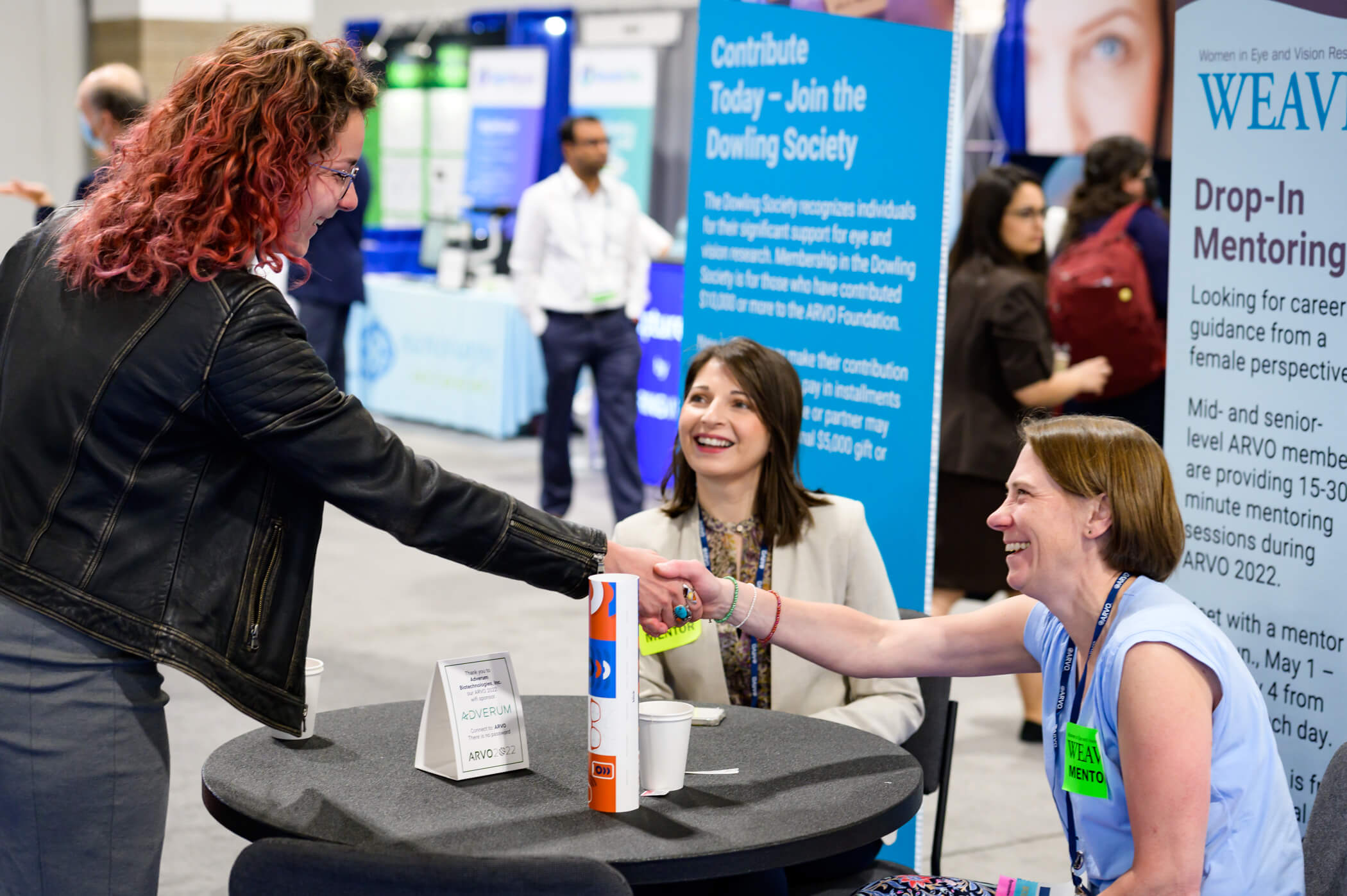 Two women sitting at a table; one shaking hands with a drop-in mentee