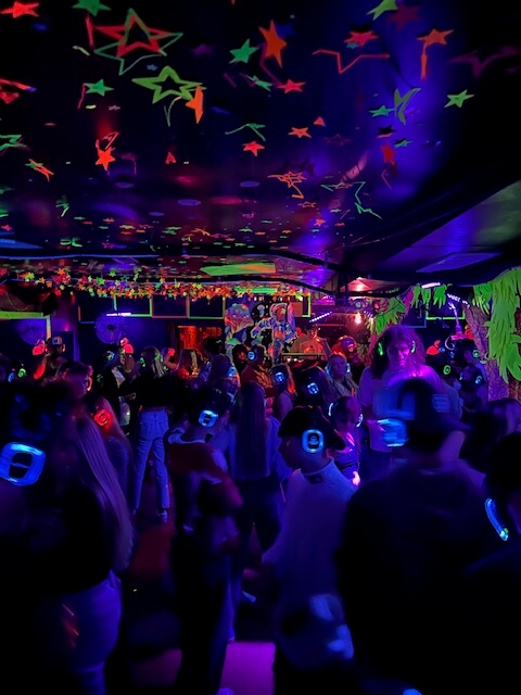 Dance floor of Why KiKi silent disco filled with dancers wearing lighted headphones under multi-colored stars reflected on the ceiling